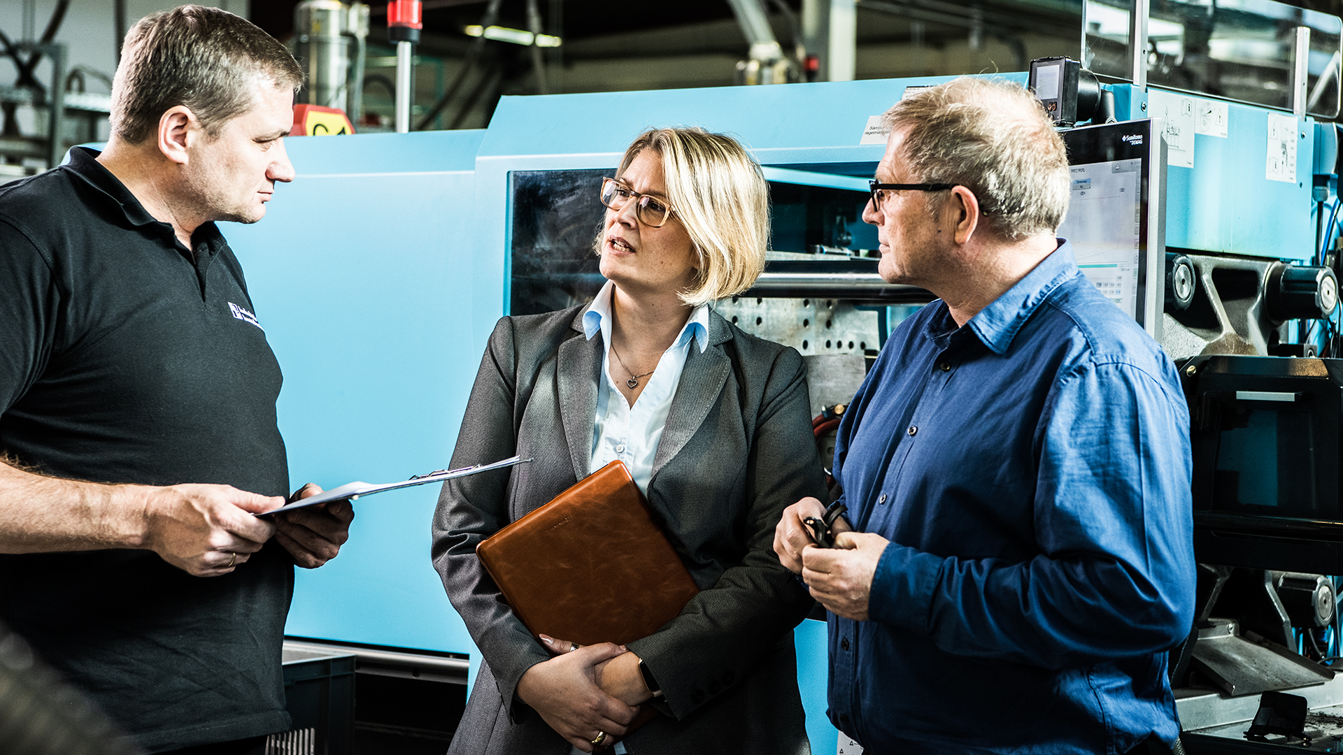 Mitarbeitende der hankensbütteler kunststoffverarbeitung im Teamgespräch vor einer Spritzgussmaschine in der Fertigungshalle